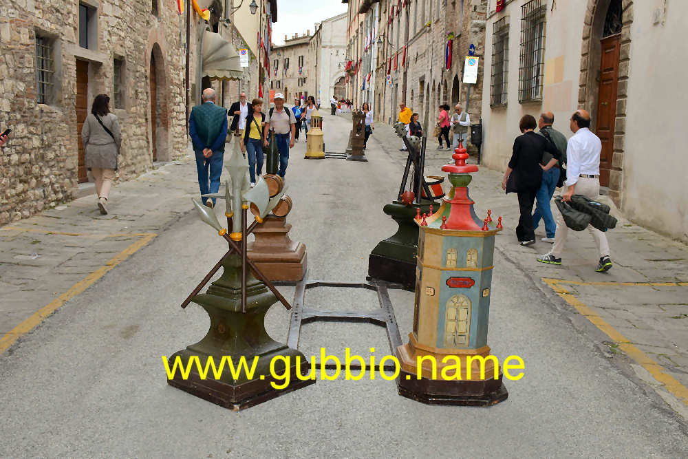 un tamburo con delle mazze, un'alabarda con le picche, dei barilotti con una bottiglia e una casa con delle botteghe